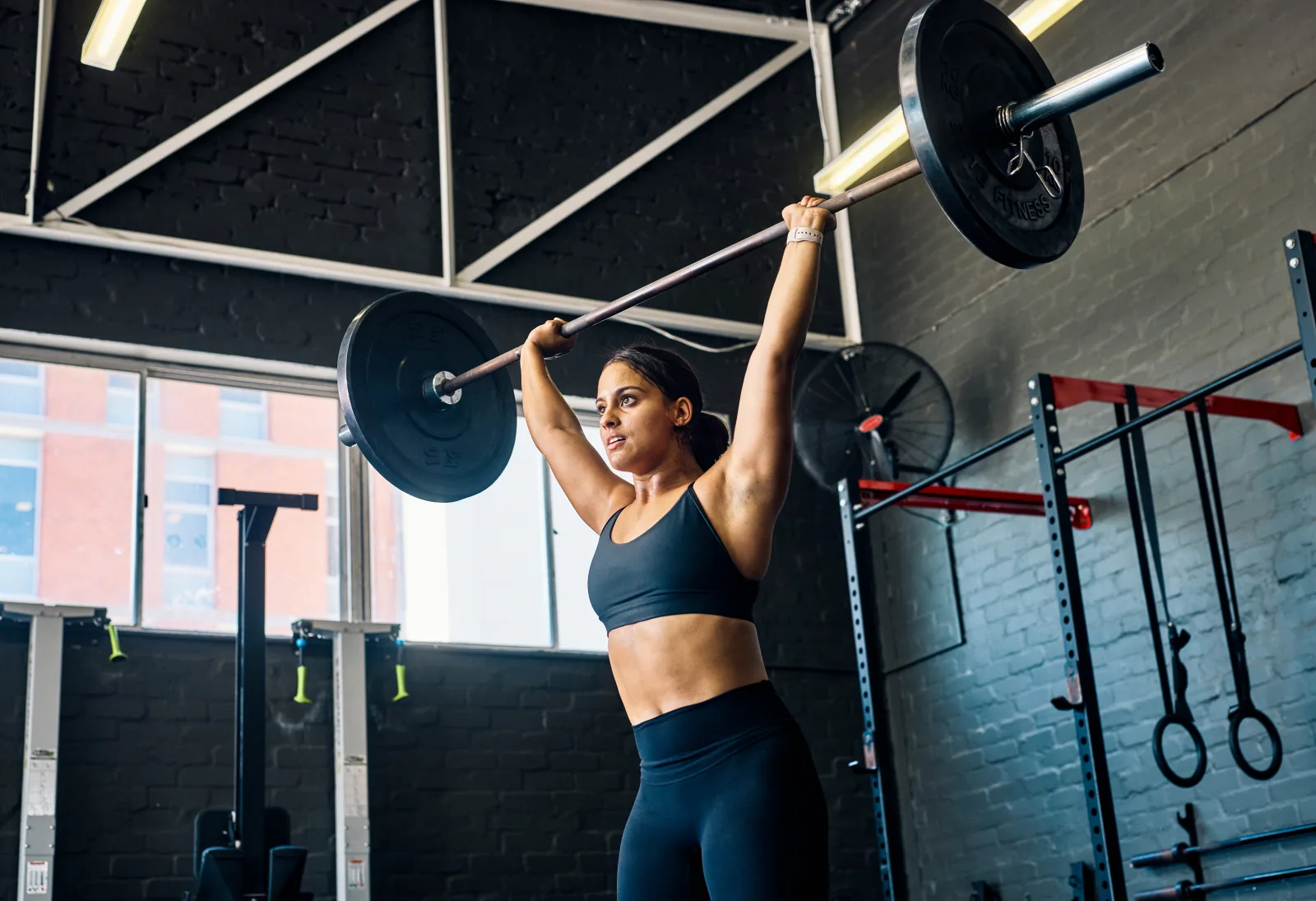 A woman lifting a barbell overhead in a gym
